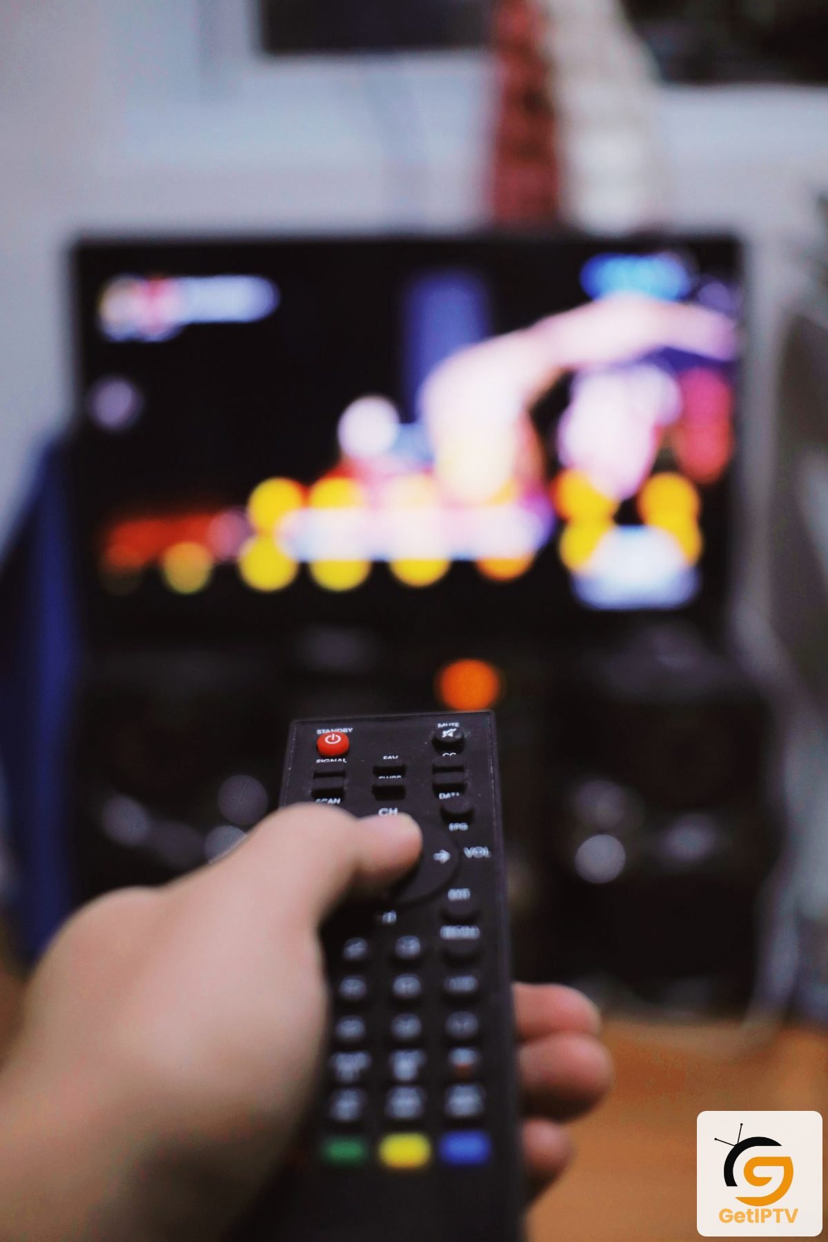 Real photo of a person using a TV remote control in a living room; GetIPTV logo added