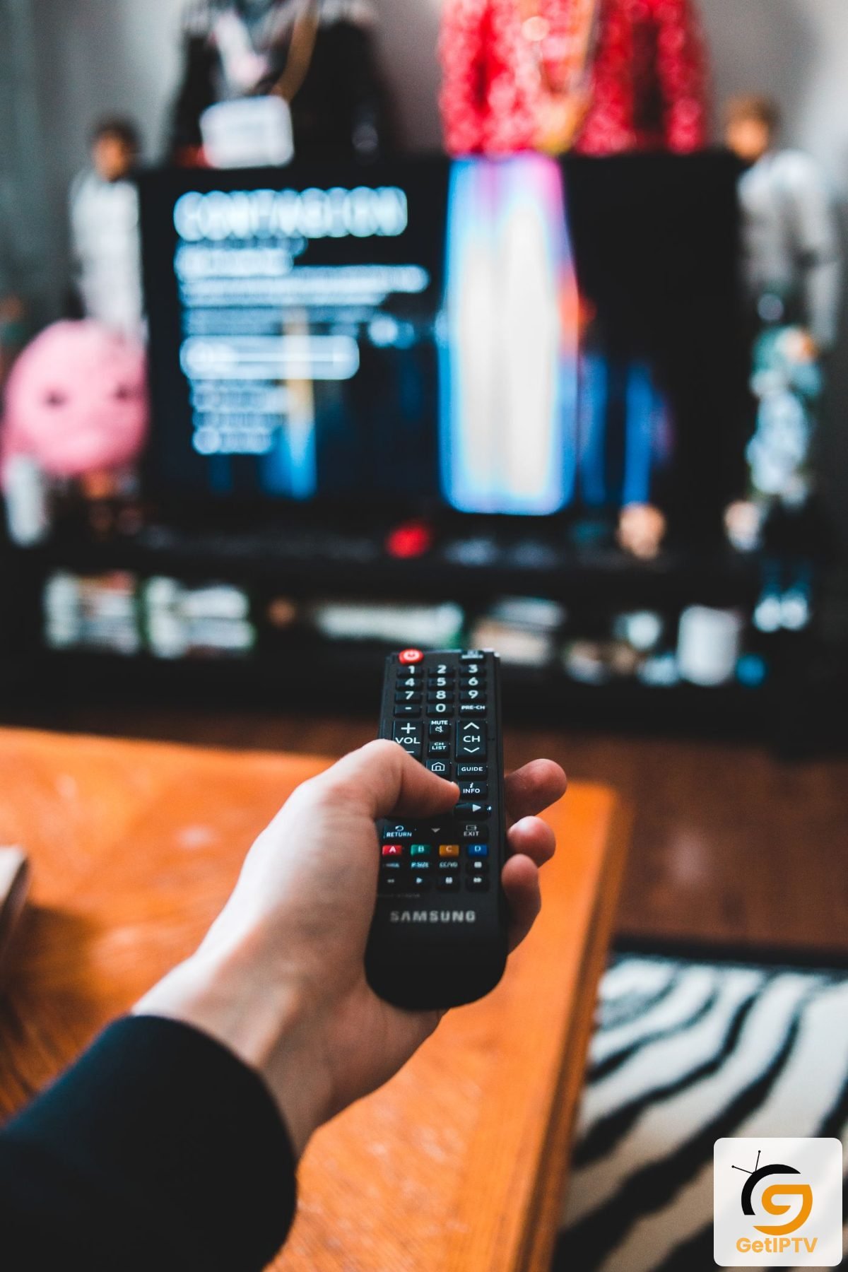 Real photo of a hand holding a Samsung TV remote in a living room; GetIPTV logo added